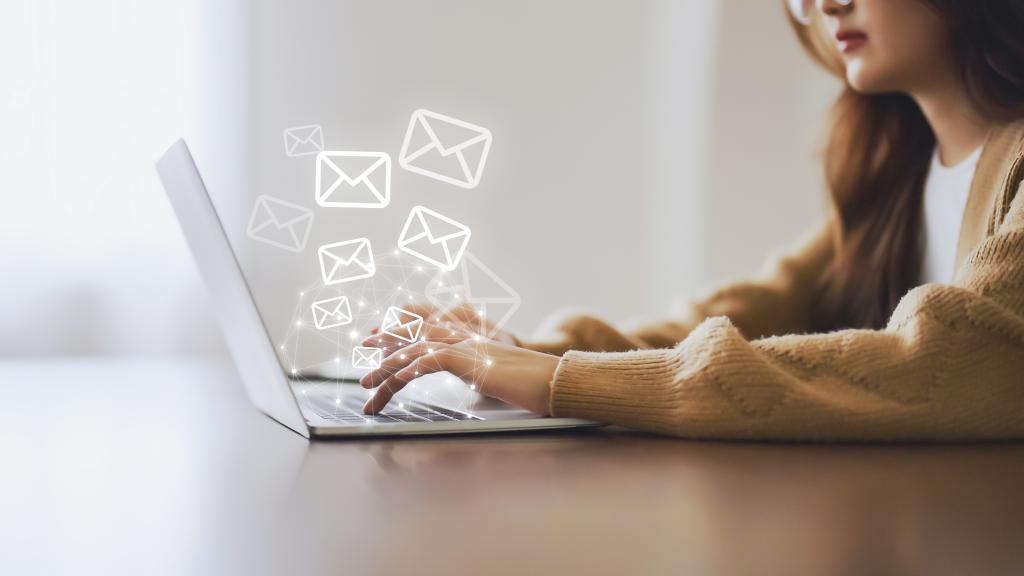 Woman sitting in front of laptop with a digital overlay of email icons coming out of the laptop.